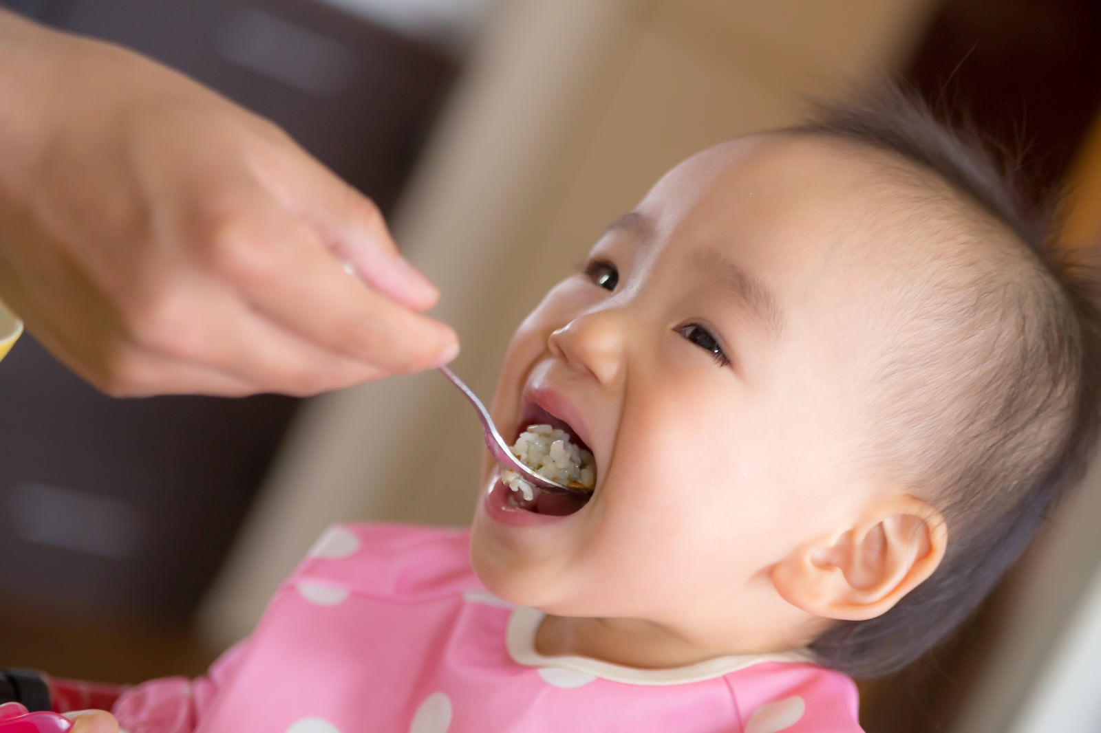 ピンク色の服を着た赤ちゃんがスプーンからご飯を食べている［モデル：あんじゅ］
