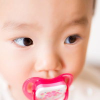 赤いおしゃぶりをくわえた赤ちゃんの顔の写真