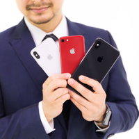 歴代iPhone三機種を手に笑顔を見せるスーツ姿のビジネスマンの写真