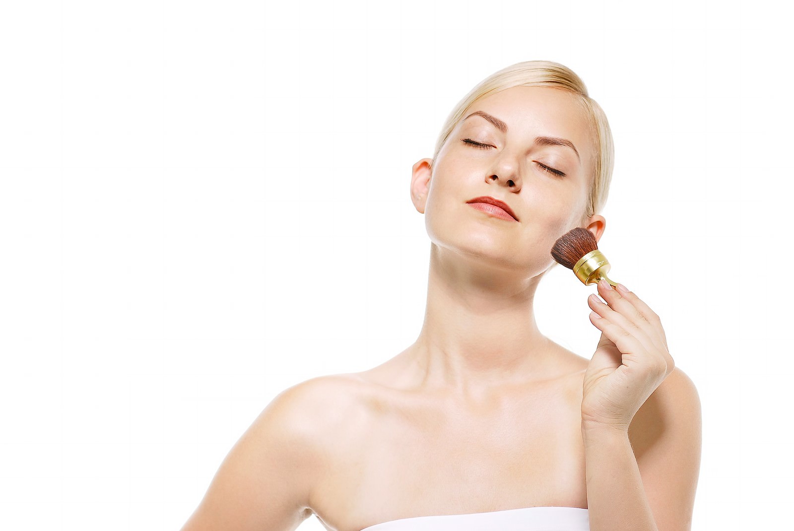 チークブラシを頬に当てる目を瞑った女性のメイク風景［モデル：モデルファクトリー］