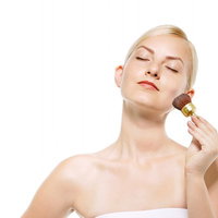 チークブラシで頬に色をのせる目を瞑った女性の写真