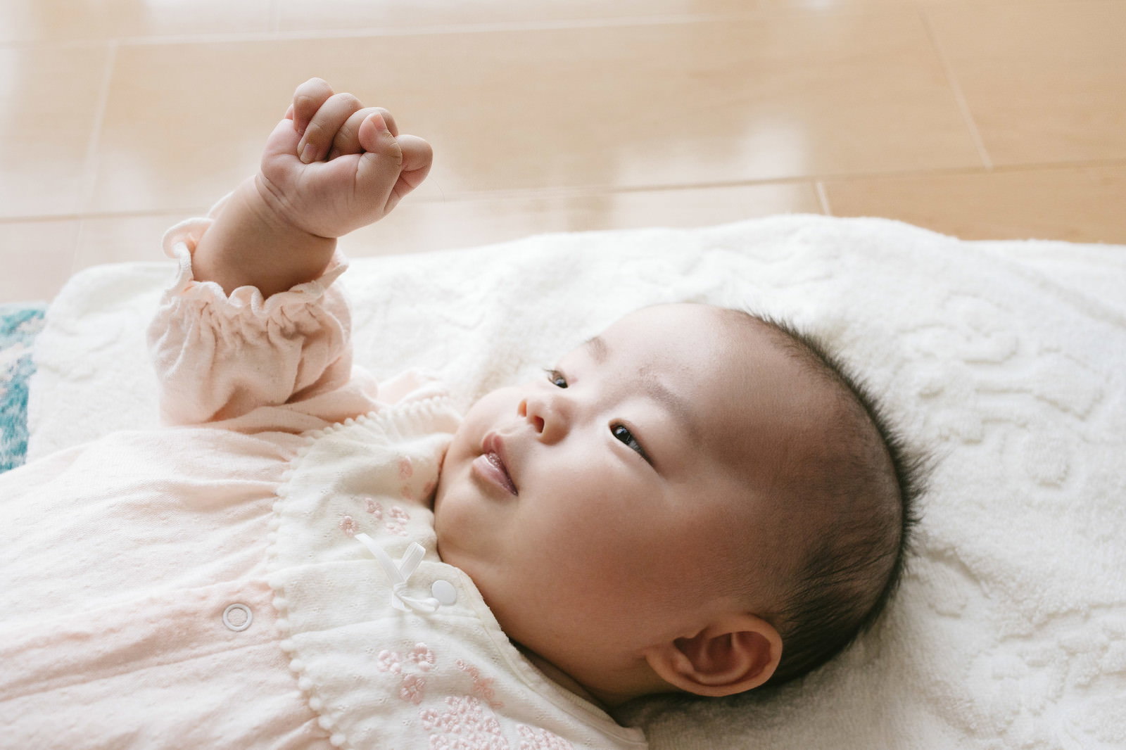 ベッドで仰向けに寝て手を上げる赤ちゃん