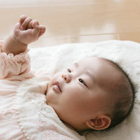ベッドの上でグーパーする乳幼児の笑顔と成長の写真