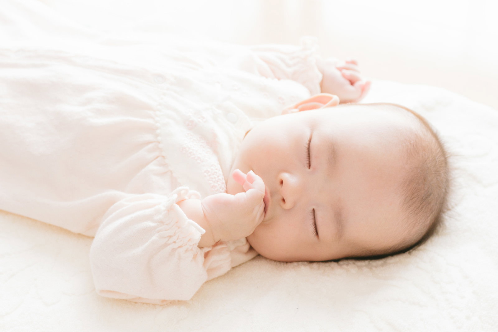 白いベビー服を着た新生児が指を咥えて眠る