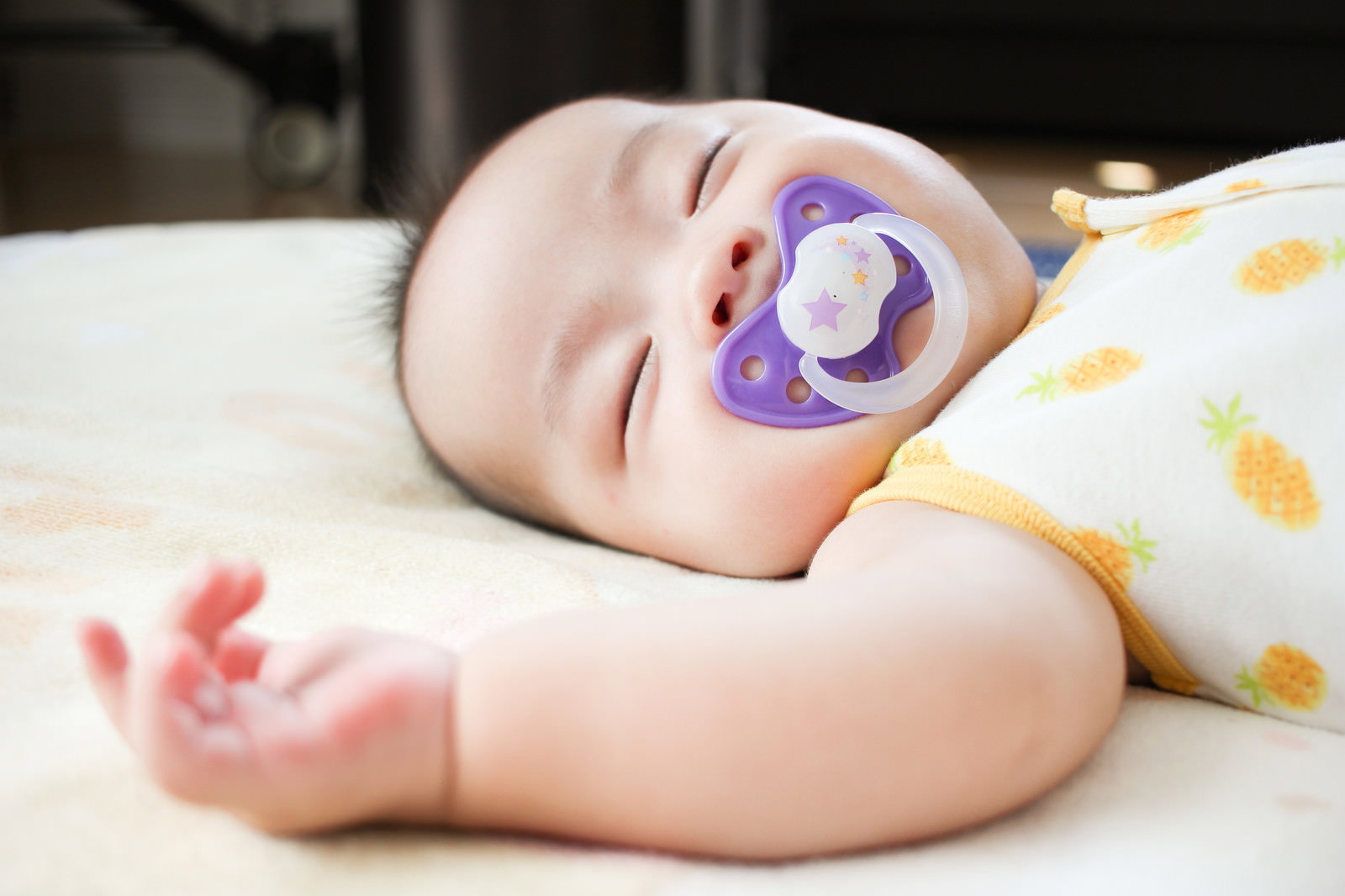 紫色のおしゃぶりを咥えて白いベッドで眠る赤ちゃん