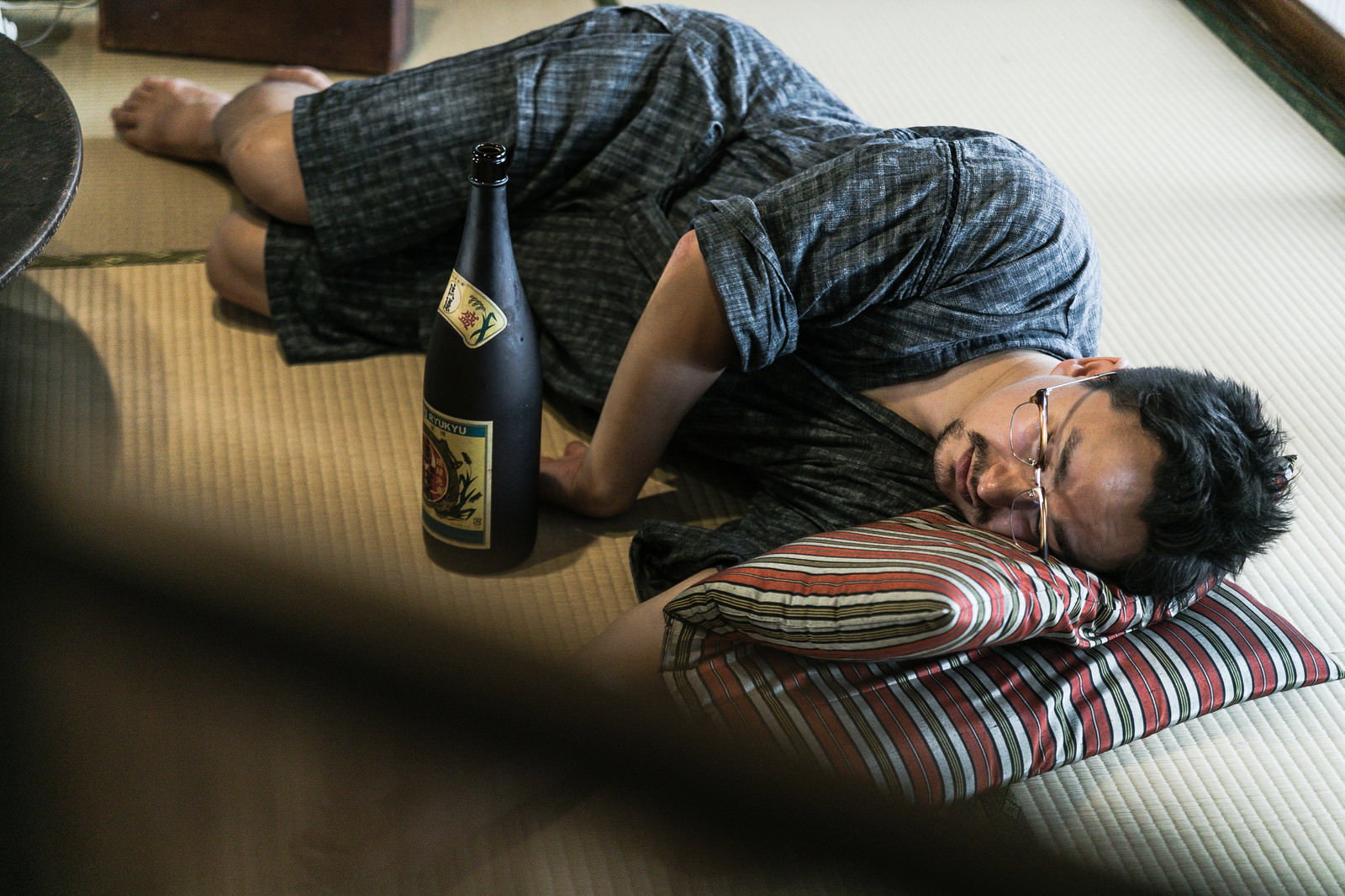 一升瓶を抱えて畳の上で泥酔して寝落ちしている男性［モデル：Max_Ezaki］