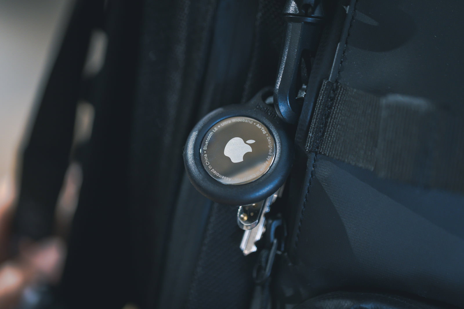 黒いバックパックのファスナーに取り付けられた白いAirTagと鍵