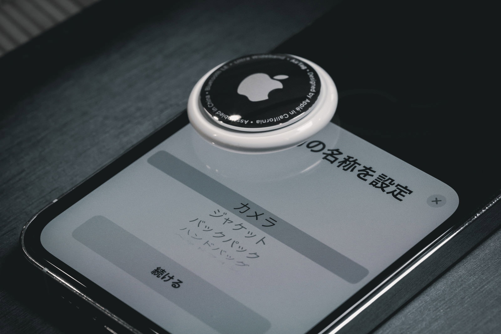 iPhoneの画面に表示されたAirTagの設定画面と白いAirTag