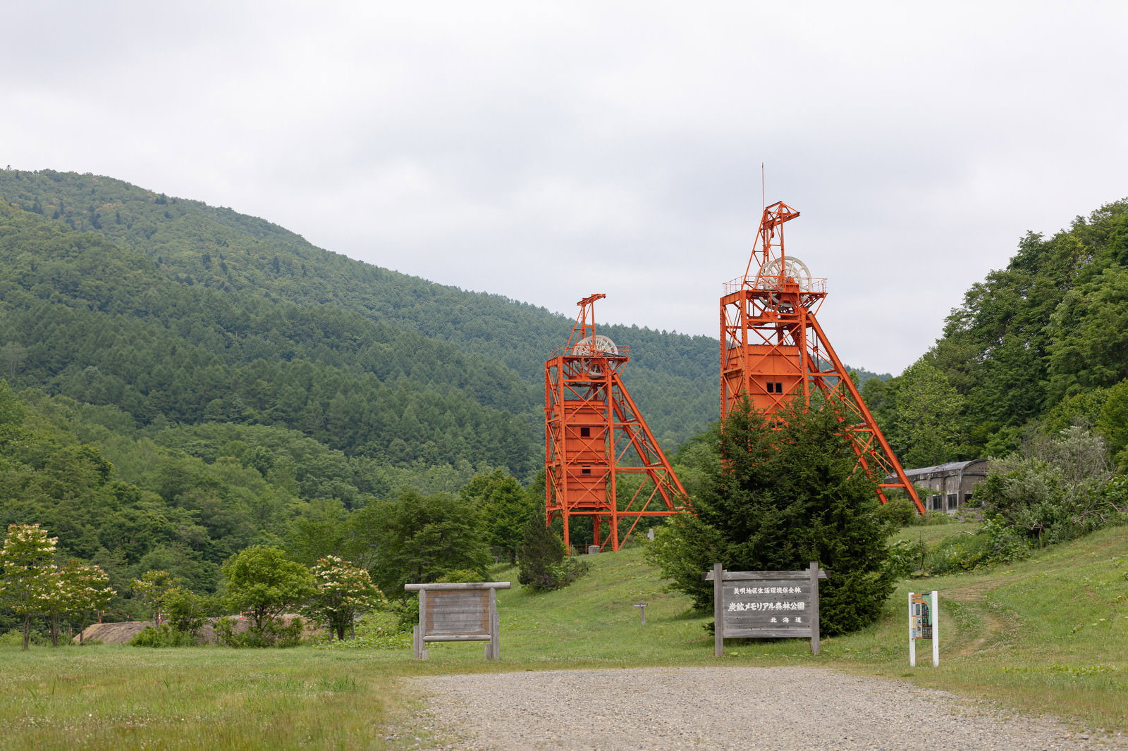 緑の森林公園に立つ赤い立坑櫓と芝生広場の風景
