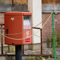 朽ちた廃墟の前に立つ赤い郵便ポスト、チェーンで囲まれた田舎の風景の写真