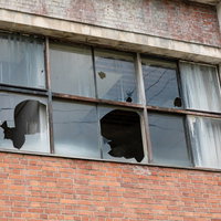 赤茶色のレンガ造りの建物に割れた窓ガラスが残る廃墟の写真