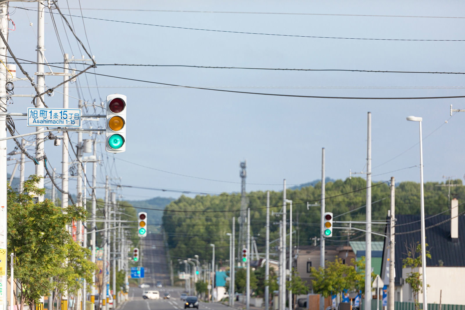 青信号が点灯する信号機と電柱が立ち並ぶ道路の風景