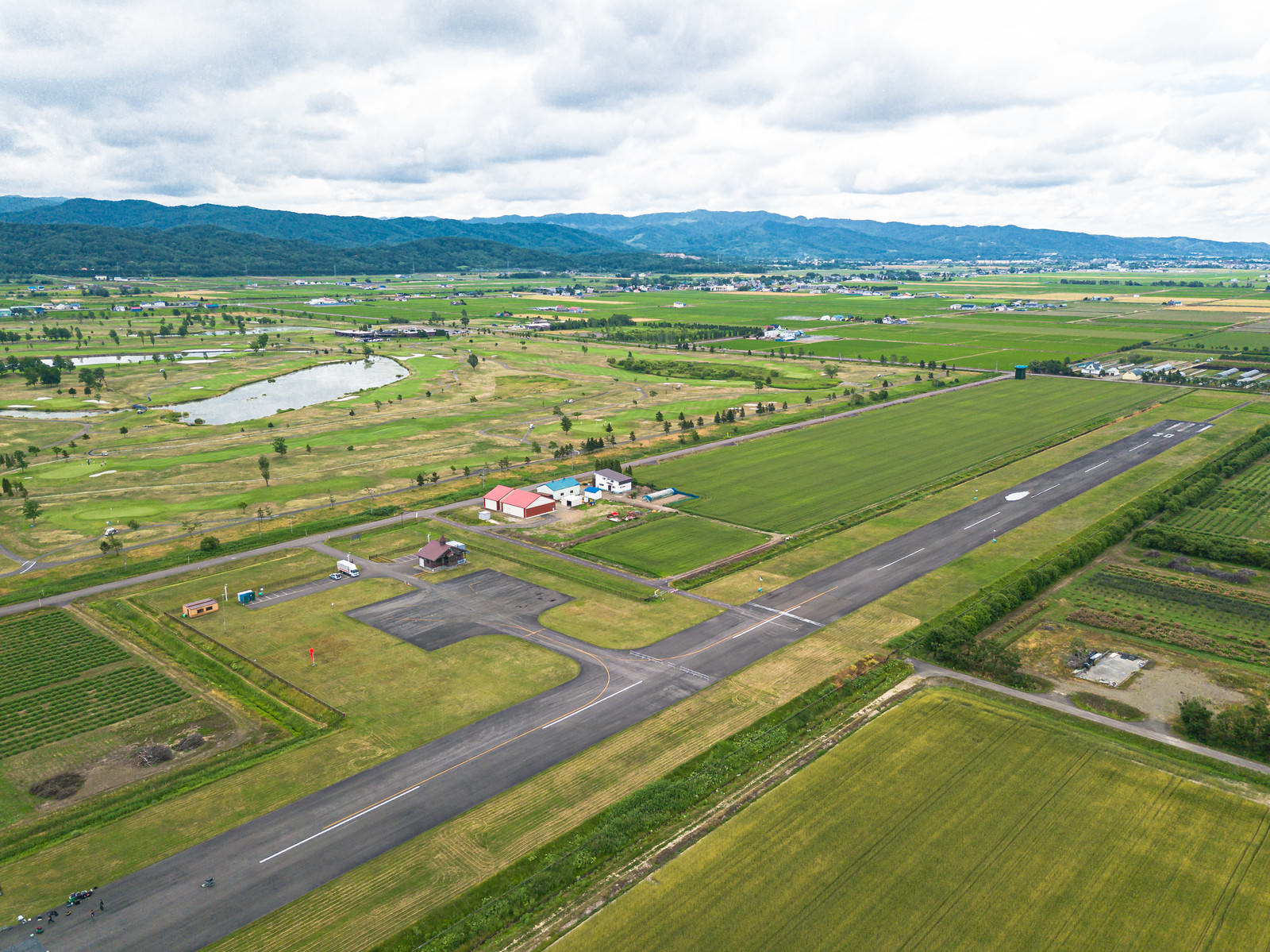 緑の田園地帯に整備された農道離着陸場の滑走路を空撮した風景