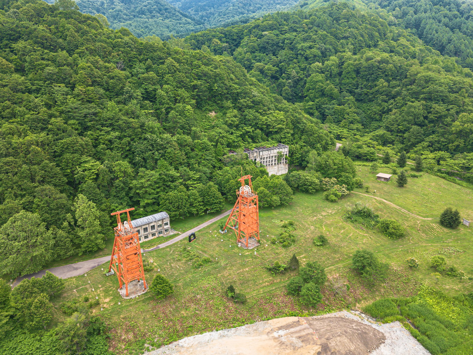 森林に囲まれた広場に建つ赤いレンガ造りの立坑櫓と原炭ポケット