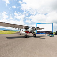 野外シネマと滑走路に駐機する小型プロペラ機の写真