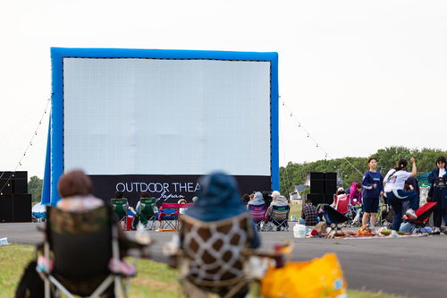 青空の下、大型スクリーンの前に集まる野外シネマ鑑賞の観客たち
