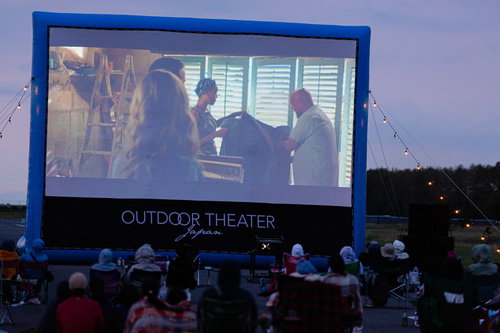 夕暮れ時のアウトドアシアター上映中、大勢の観客が野外映画を鑑賞