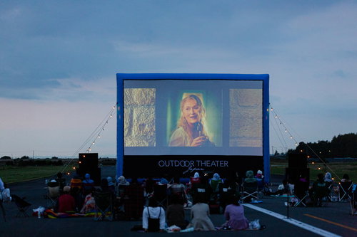滑走路に設置された巨大スクリーンで野外映画を楽しむ町の人々