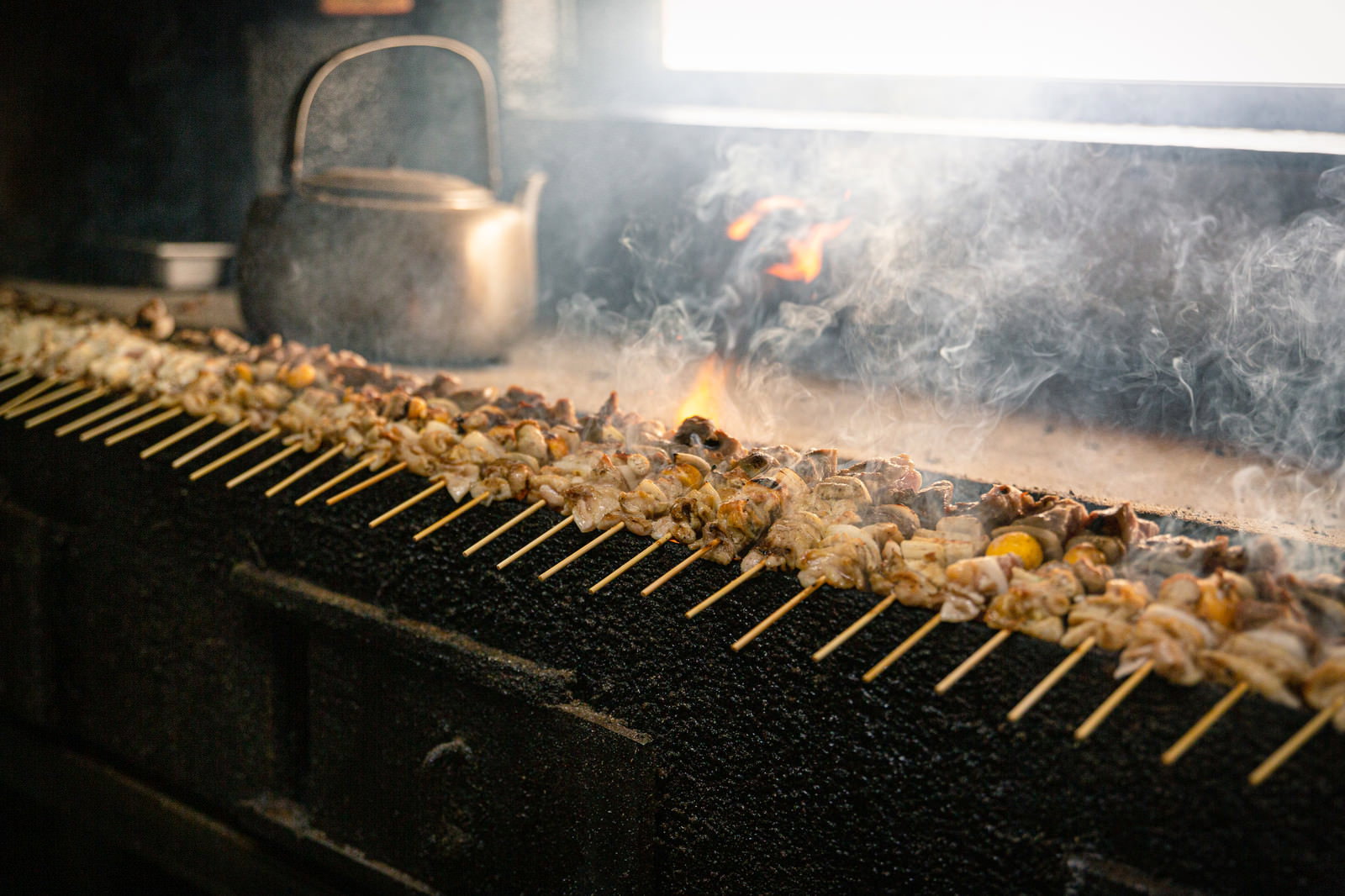 炭火の上で焼かれている美唄焼き鳥の串、煙が立ち上っている様子
