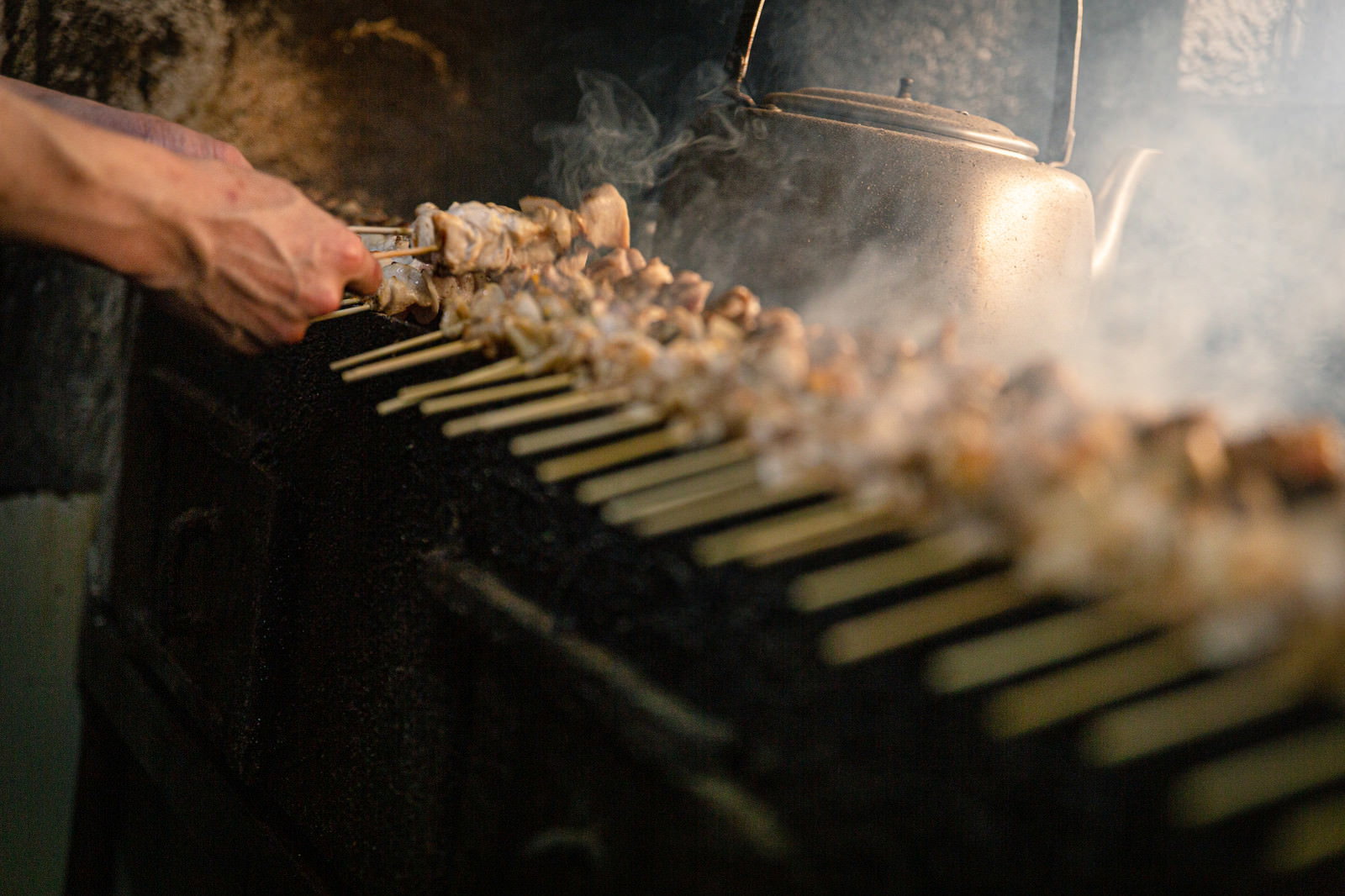 炭火の上で焼き鳥を調理する手と立ち上る煙
