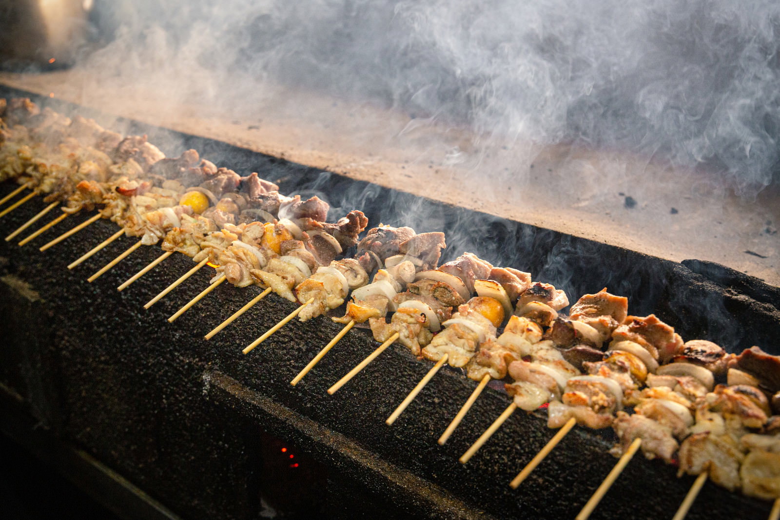 炭火の上で焼かれている美唄焼き鳥の串、煙が立ち上る様子