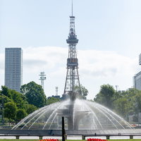 噴水越しに見るさっぽろテレビ塔と大通公園の札幌市街地の写真