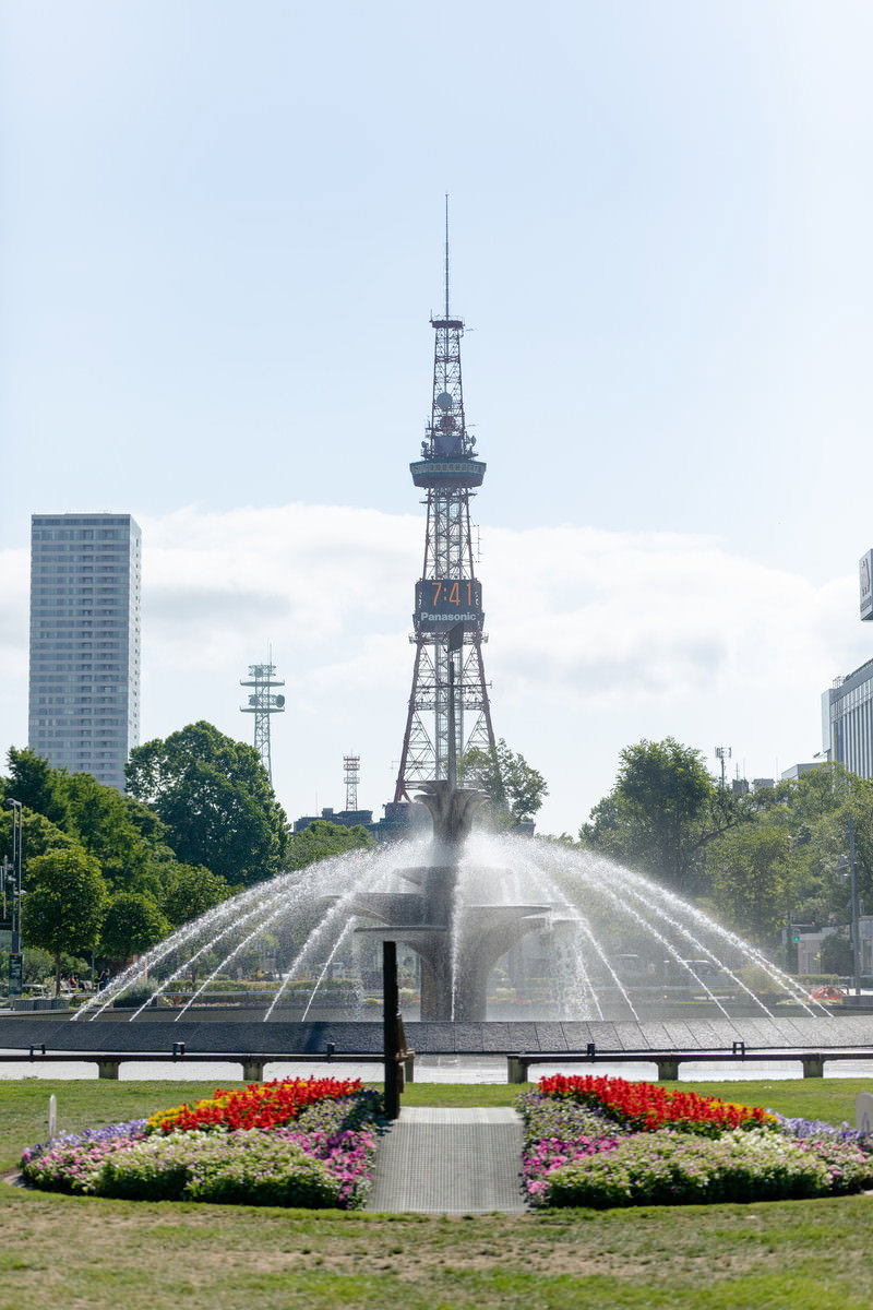 大通公園の噴水越しに見るさっぽろテレビ塔と札幌市街地の風景