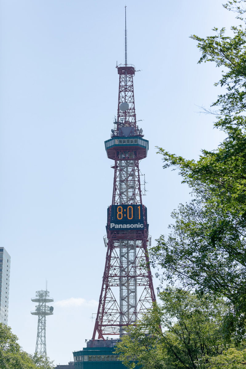 緑の木々に囲まれた大通公園のさっぽろテレビ塔、電光時計が8時1分を表示