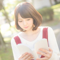 午後、赤いスカートで読書日和。白いニット長袖の女性が屋外で本を読むの写真