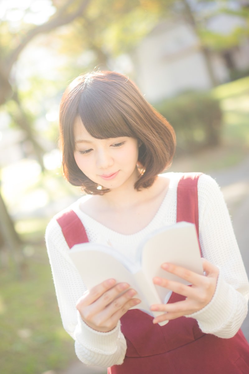 赤いスカートをはいた女性が屋外で本を読んでいる［モデル：みき。］