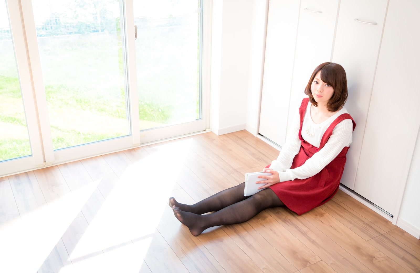 床に座って漫画を読む赤いベストの女性［モデル：みき。］
