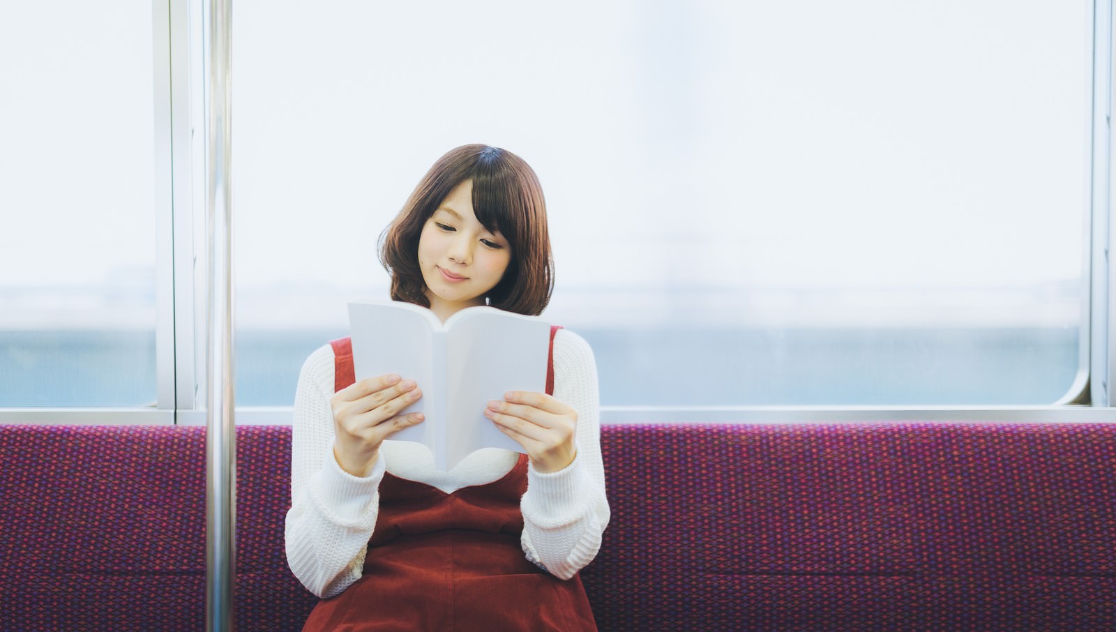 電車のシートに座り、本を読む女性［モデル：みき。］