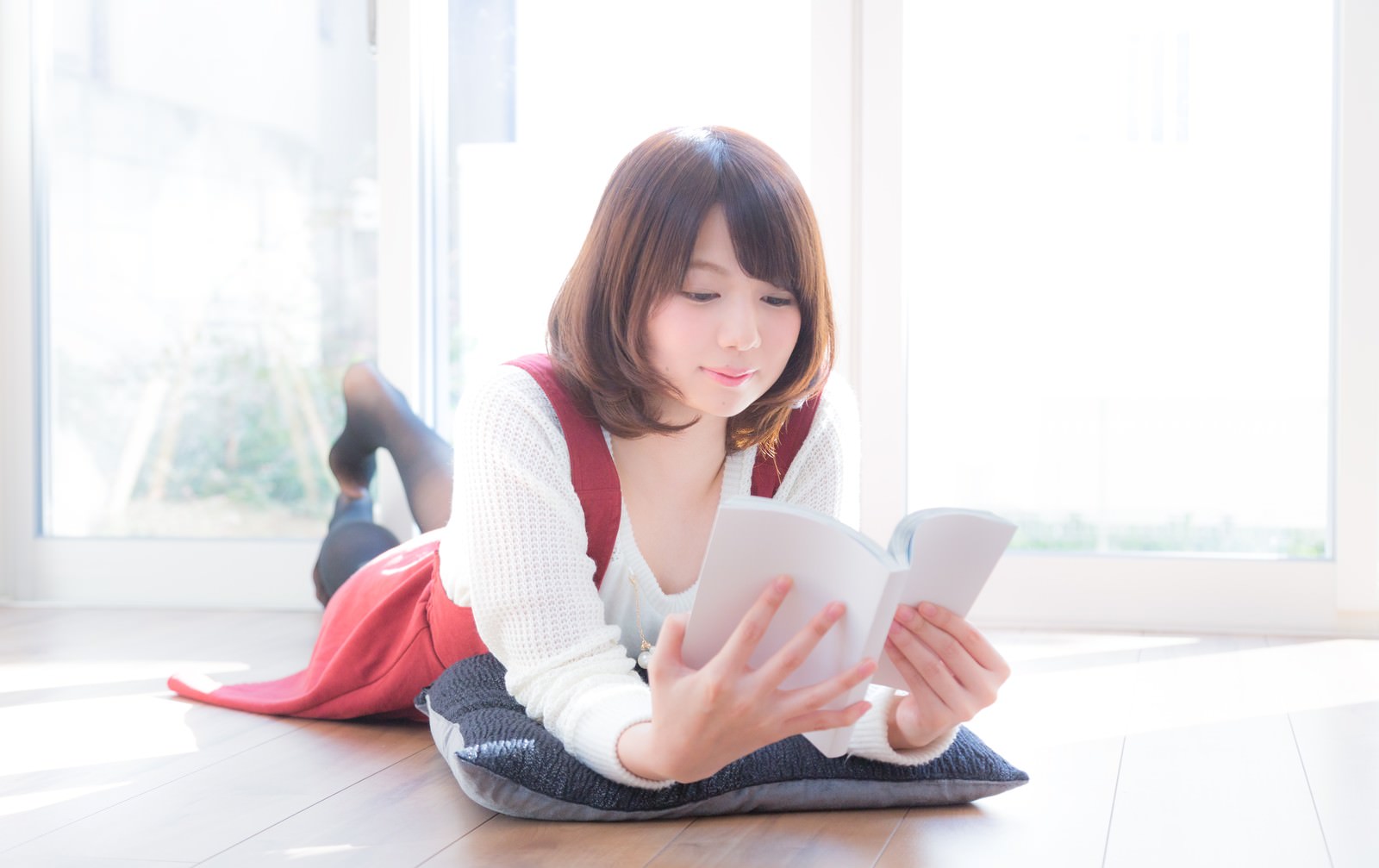 リビングで寝転んで漫画を読むワクワクした表情の女性［モデル：みき。］