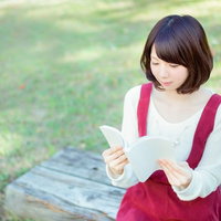 公園のベンチで本を読む女性、白いニット姿でリラックス読書の写真