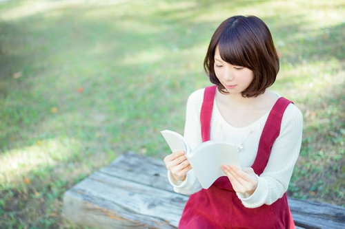 公園のベンチで本を読む女性、白いニット姿でリラックス読書