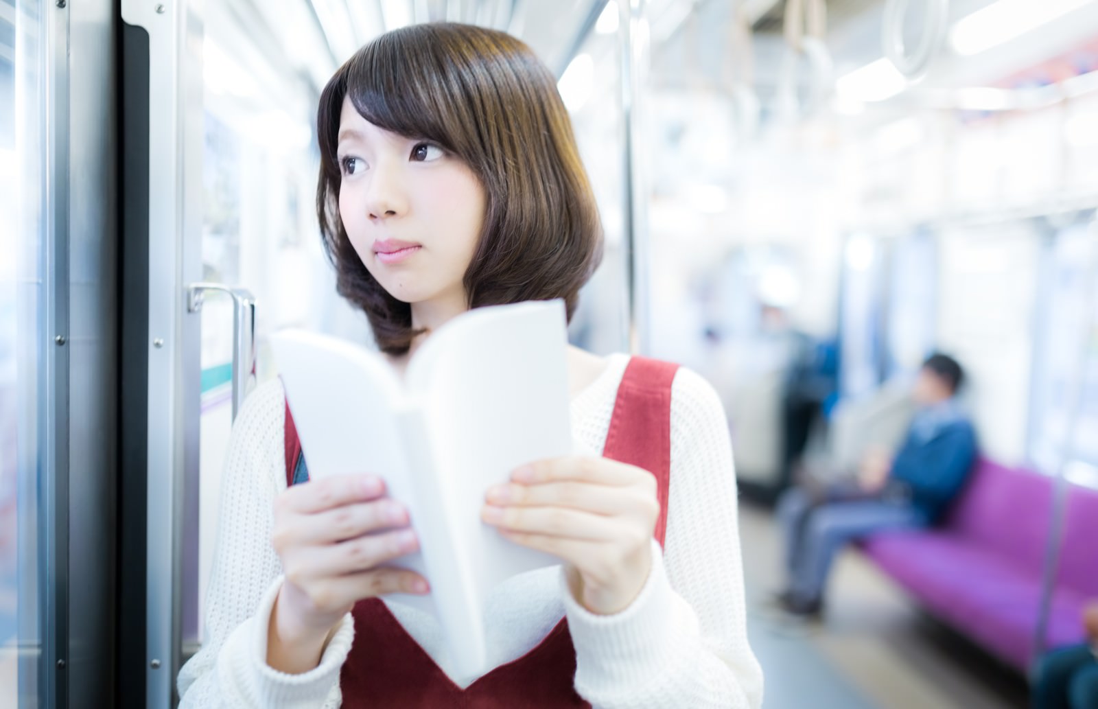 電車の中でマンガを読む白いニットベストの美少女［モデル：みき。］