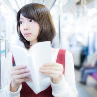 電車の中でマンガを読む美少女、ベージュベストと白いニット帽姿の写真