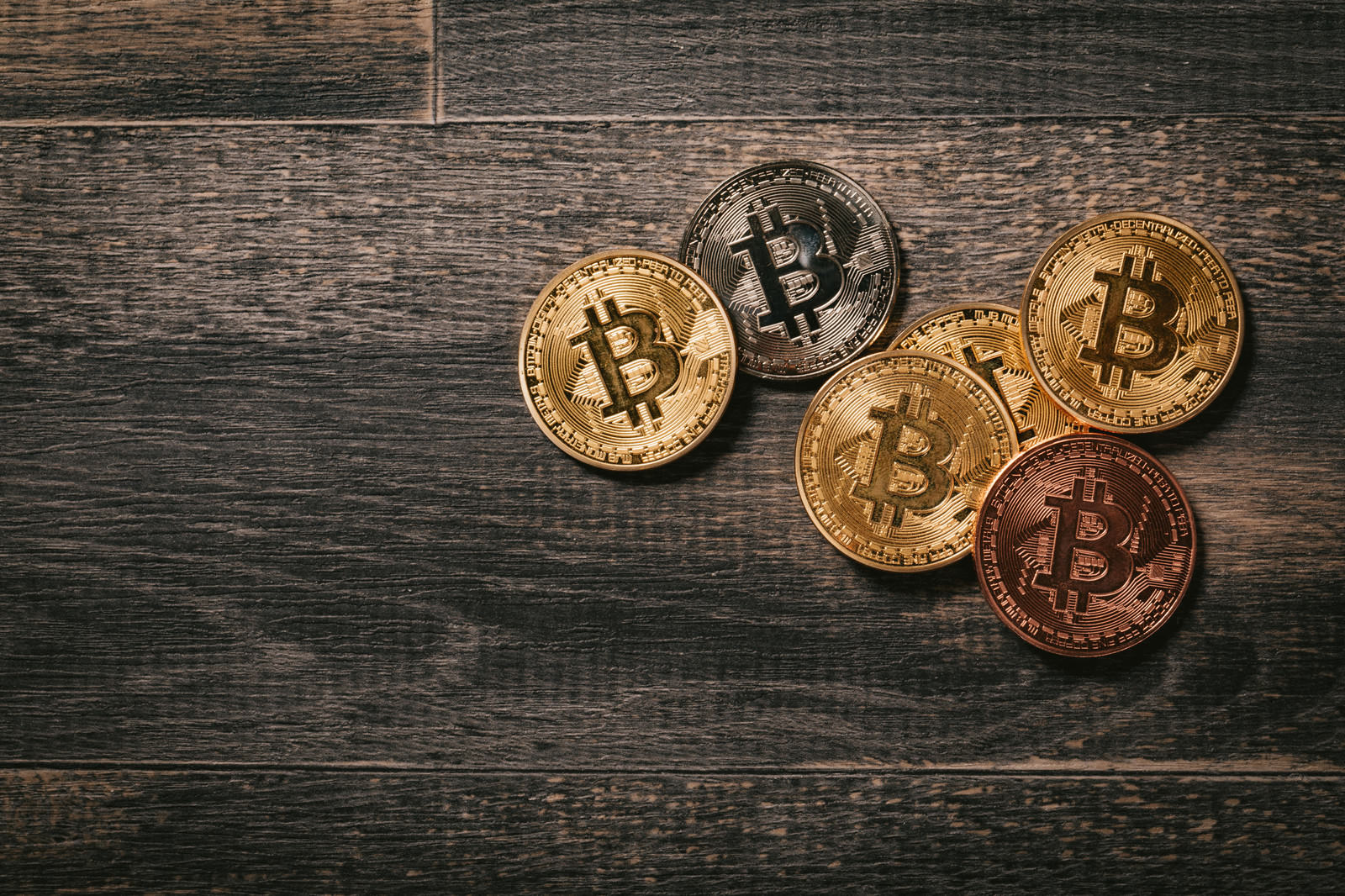 木目の板の上に金色と銅色のビットコインのメダルが複数枚配置されている
