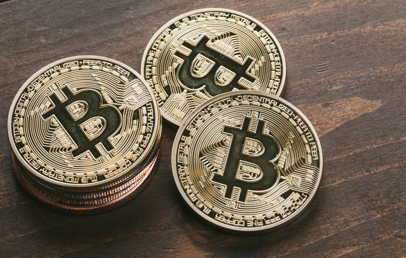 木製テーブルの上に重なる金色のビットコインコイン3枚