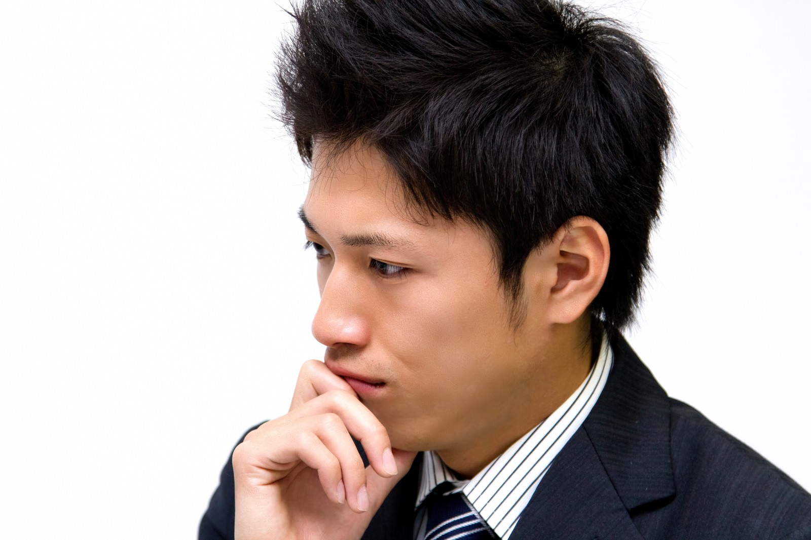 口元に手を当てて考えるスーツ姿の男性［モデル：恭平］