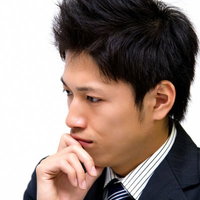 口元に手を当てて考えるスーツ姿の男性の写真