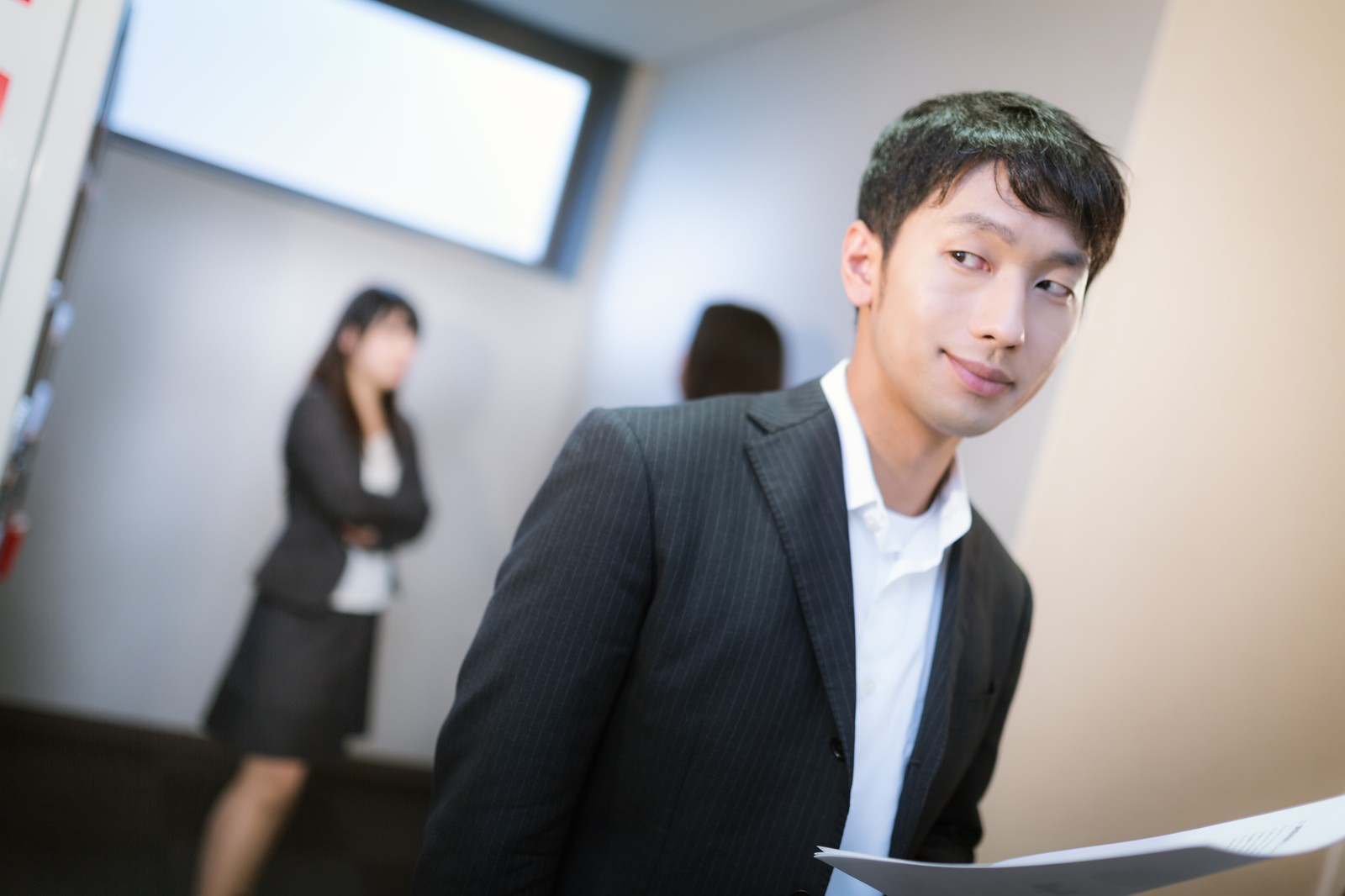 オフィスで女性社員の話を聞く濃紺スーツ姿の男性社員［モデル：大川竜弥 Lala］