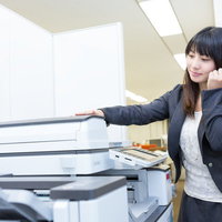 オフィスで複合機の蓋を開けて操作するスーツの女性の写真