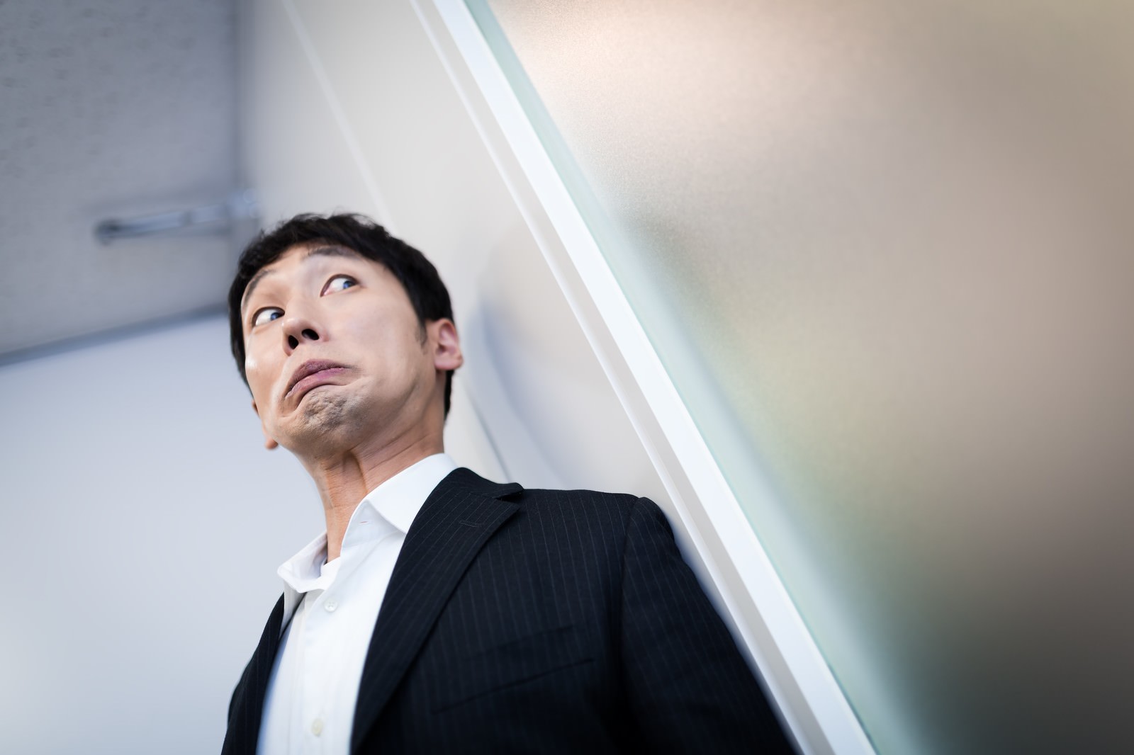 驚いた表情で上を向く黒いスーツの男性ビジネスパーソン［モデル：大川竜弥］