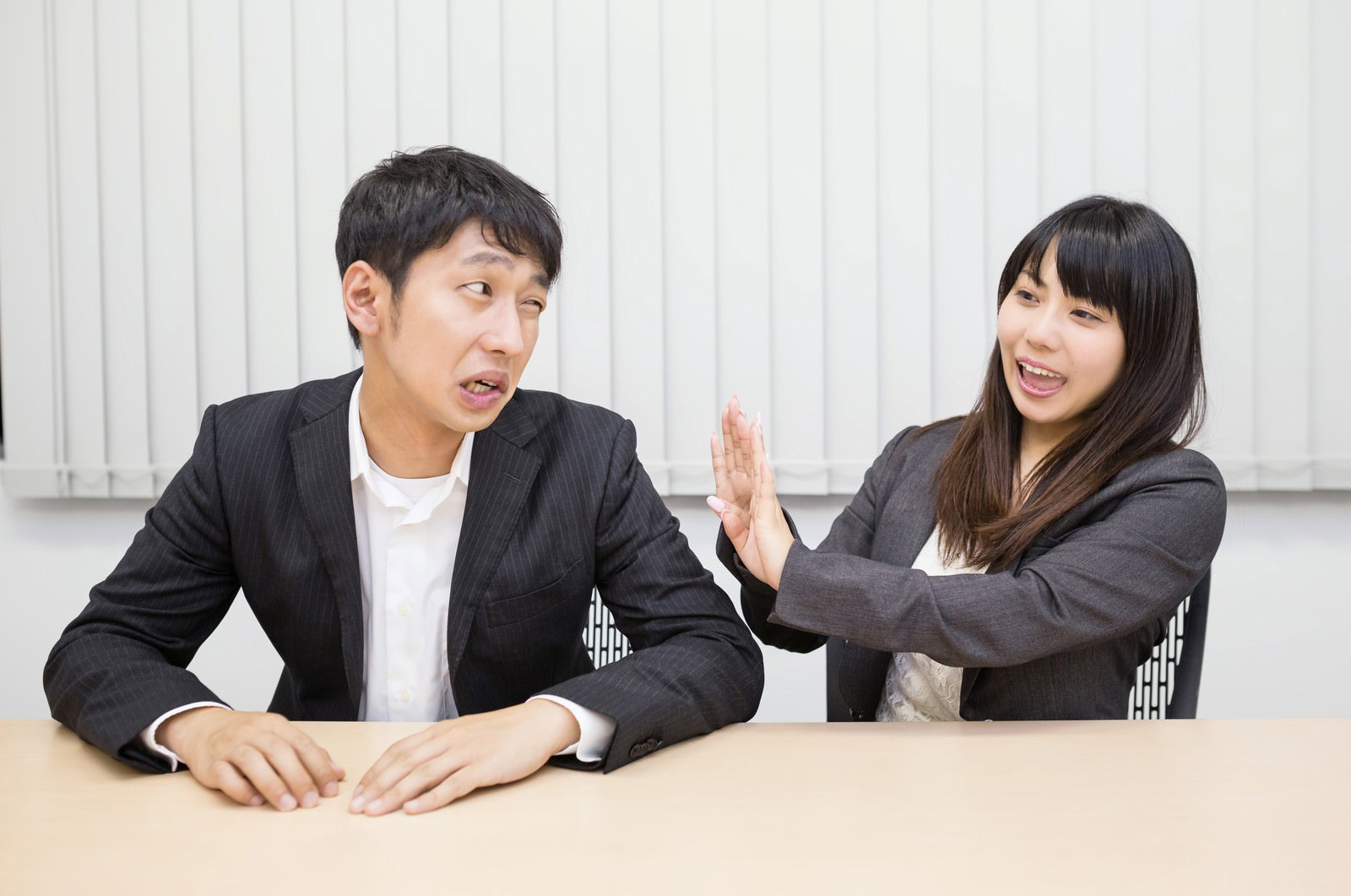 会議中に男性上司から手を上げて顔を背ける濃紺スーツの女性社員［モデル：大川竜弥 Lala］