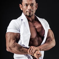 白衣のままサイドチェストポージングを披露する男性ボディビルダーの写真