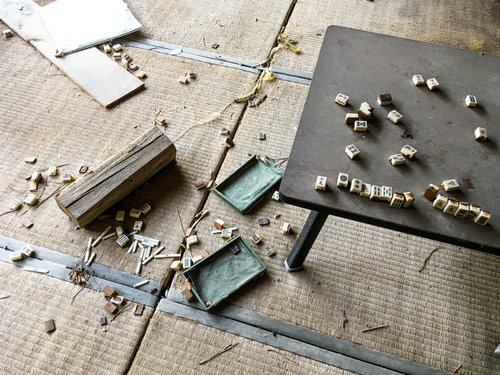 廃屋の和室に散らばった麻雀牌と破れた障子