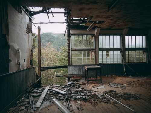 朽ちて倒壊しそうな廃校の教室の中、天井が大きく崩れ落ちた荒廃した室内