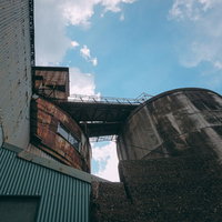 青空の下で錆びついた渡り通路と工場タンクの写真