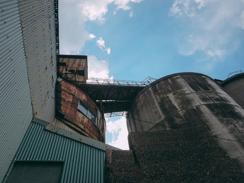 青空の下で錆びついた渡り通路と工場タンク